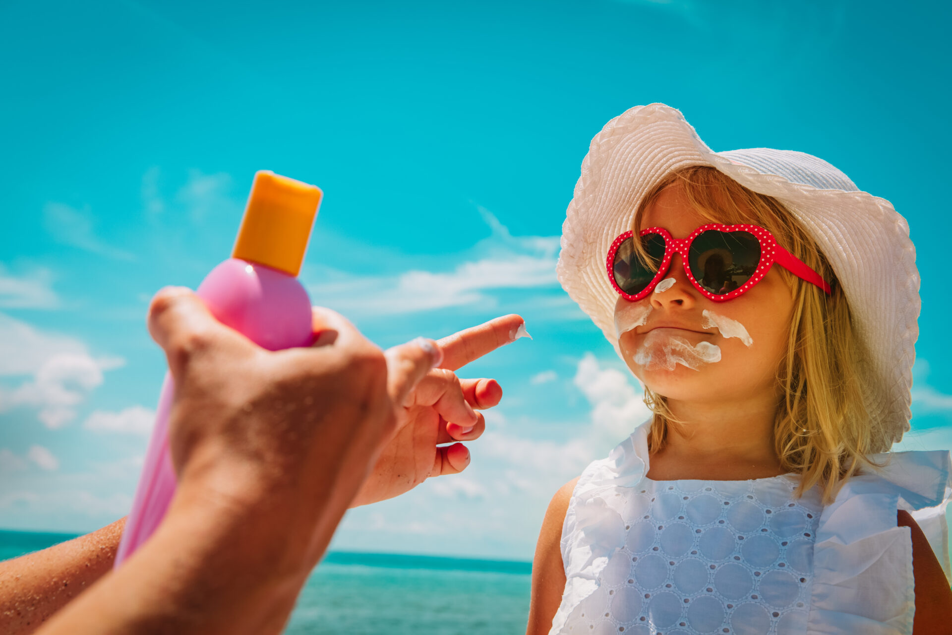 sun protection - mom put suncream on little girl face at beach